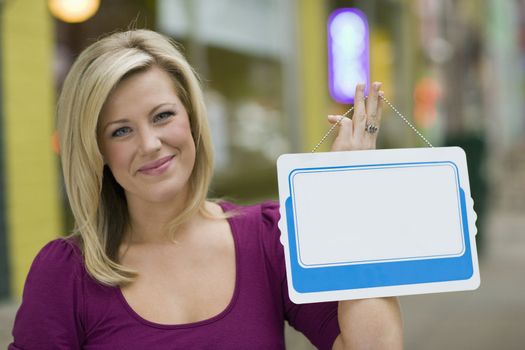 Pretty blond woman holding up a blank white sign with urban background