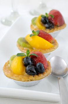 Individual small fruit tarts, filled with custard and decorated with a strawberry, blueberries, kiwi and mango slices