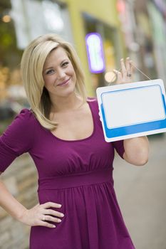 Pretty blond woman holding up a blank white sign with urban background