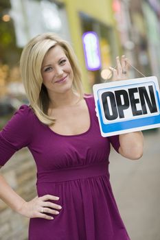 Pretty blond woman holding up an open sign with urban background
