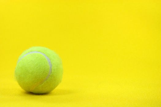 one yellow tennis ball in the left side with yellow background sports concepts