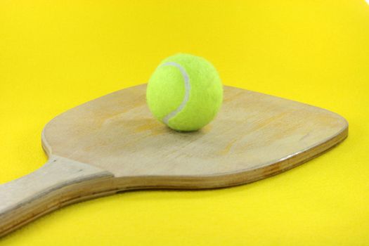 beach wooden racket with yellow ball in yellow background prespective