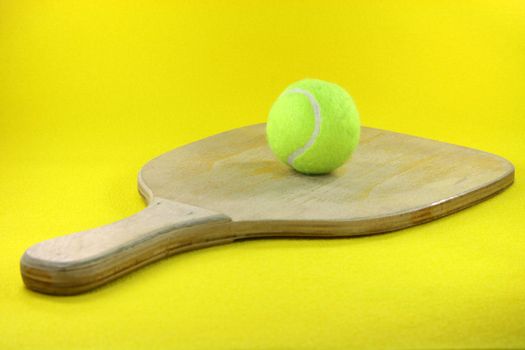 beach wooden racket with yellow ball in yellow background prespective