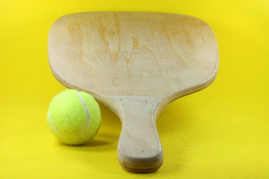 beach wooden racket with yellow ball in yellow background