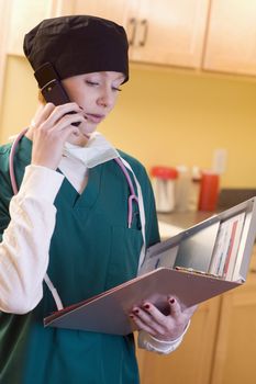 Medical professional wearing surgical gear holding medical chart and talking on cell phone