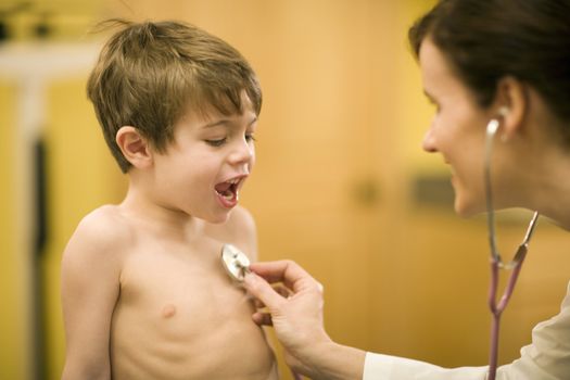 Woman doctor using a stethoscope on talkative boy patient