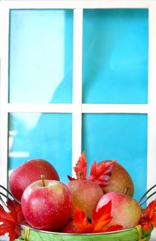Basket of apples and fall leaves in front of a fake window. Copy space available.