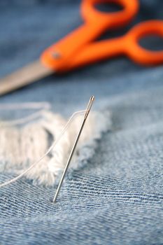 Close up of a needle and thread with scissors in the background.