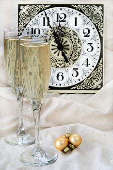 Wine glasses and ornaments with a clock in the background showing that it is almost midnight.