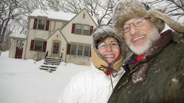 Happy senior couple standing in front of house in winter
