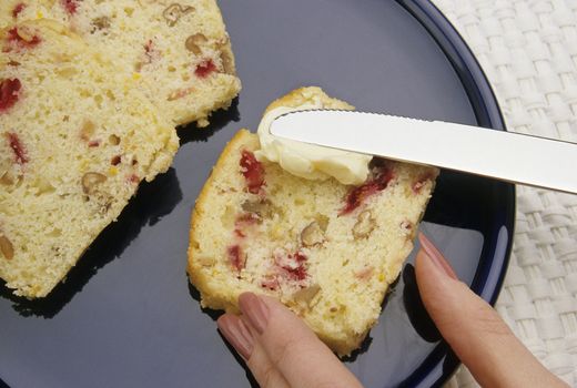 Hand spreading butter on fruit bread
