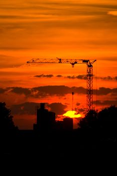  crane with a  sunset and silhouette of a factory in the back 