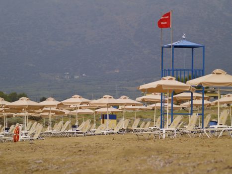 empty beach in greece, red flag on lifeguards tower