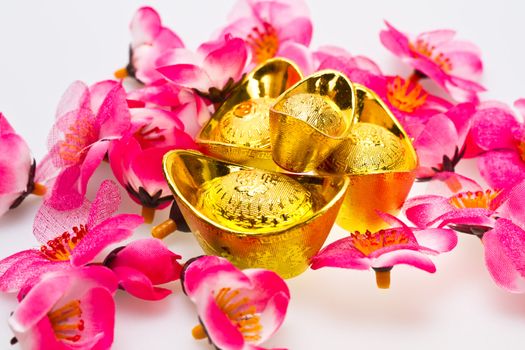 Angled view of Chinese golden ingots with cherry plum blossoms on white surface