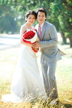 couples portrait of bride and groom on beautiful meadows with rose bouquet