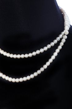 Double string of matched pearls displayed around the neck of a black mannequin
