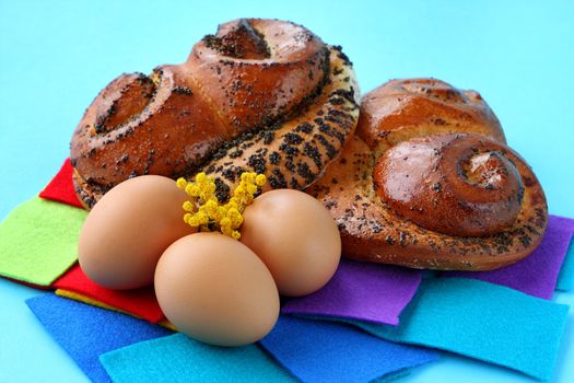 Buns with poppy seeds and brown eggs on blue background