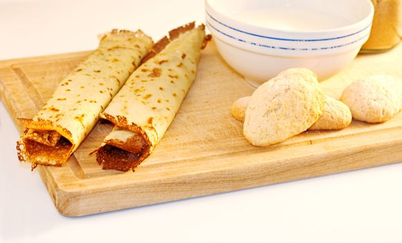 Crepes, cookies and milk on cutting board