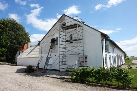 Man on scaffolds painting a house during exterior renovations                               