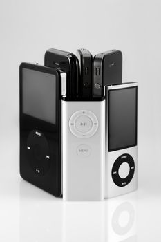 A studio shot of a collection of apple products including two iphone 4's, one iphone 3GS, a 5th generation 30GB ipod, a 5th generation 16GB ipod nano, and a apple itunes controller.