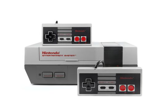 A studio shot on a solid white background of a Nintendo Entertainment System and two Nintendo controllers.