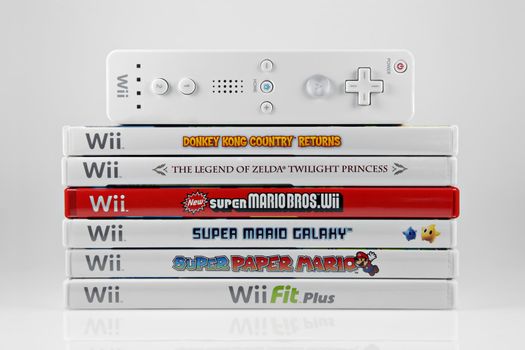 A studio shot of a stack of 6 Nintendo Wii video games and controller. Games include Donkey Kong Country Returns, The Legend of Zelda Twilight Princess, New Super Mario Bros. Wii, Super Mario Galaxy, Super Paper Mario, and Wii Fit Plus.