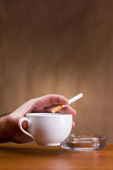 Hand holding a cigarette and a cup ashtray.