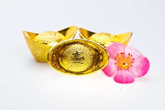 Three chinese gold ingots and cloth cherry plum blossoms for new year celebration on white surface