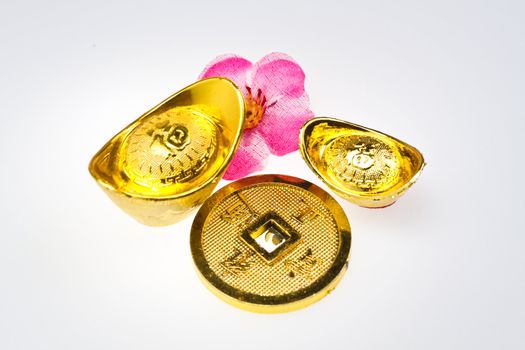 Gold ingots and Chinese Emperor's coin with artificial cherry blossom on white surface