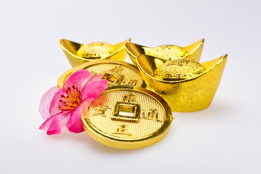 Gold ingots and Chinese Emperor's coin with artificial cherry blossom on white surface