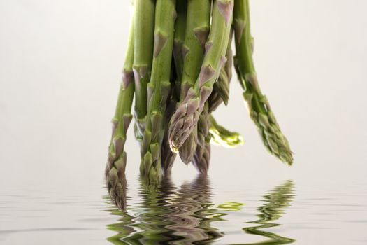 A bunch of asparagus reflected in water on a gray background
