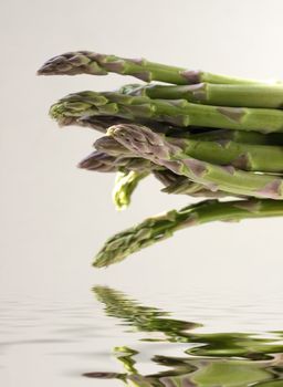 A bunch of asparagus reflected in water on a gray background