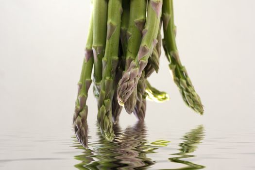 A bunch of asparagus reflected in water on a gray background