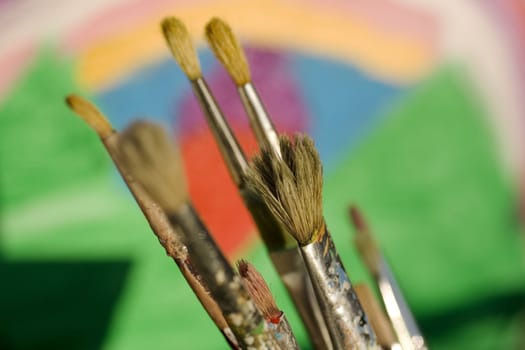 Paintbrushes and painted canvas in the background