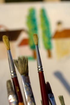 Paintbrushes and painted canvas in the background