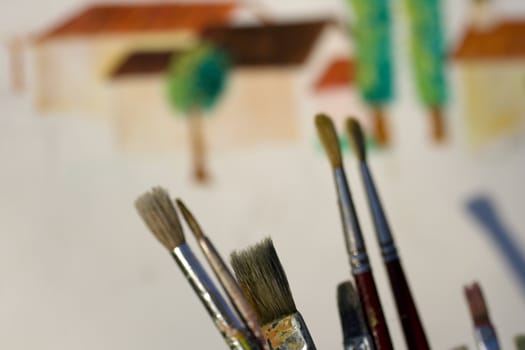 Paintbrushes and painted canvas in the background
