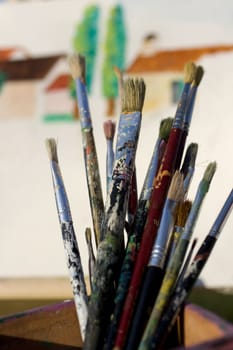 Paintbrushes and painted canvas in the background