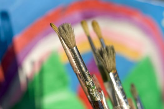Paintbrushes and painted canvas in the background