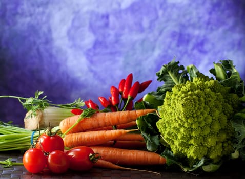 Roman cauliflower, carrots, tomatoes and other vegetables on purple background