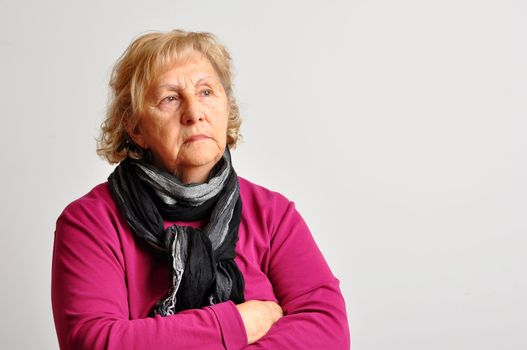Blond senior woman with crossed arms deep in her thoughts over light grey background.