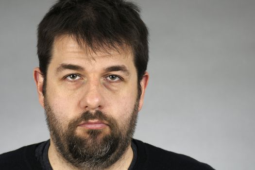 Portrait of a very serious, somber or depressed dark hair and beard middle-age man over grey bacground.