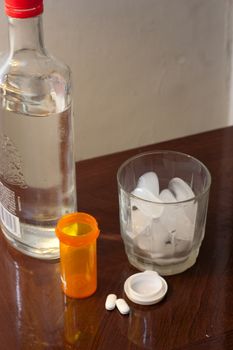 Glass of ice and a liquor bottle with pills and empty bottle.