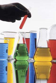 Hand holding test tube with various colorful science glassware