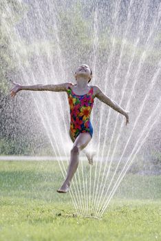 Young girl with a joyful expression jumping through a spray of water