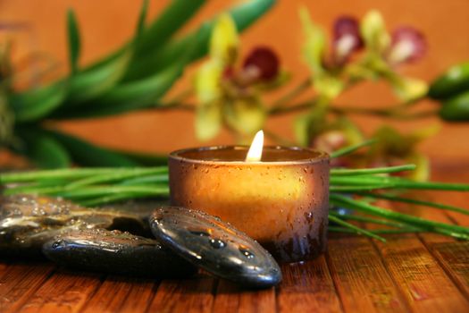 Amber candle and spa stones with orchid  on bamboo