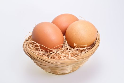 Three brown eggs in rattan basket with straw bedding on white background