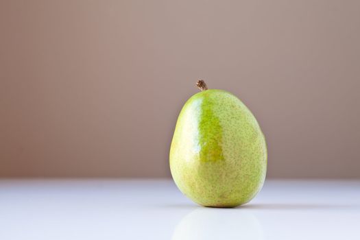 Single green pear on white table with taupe brown background. Concepts: nutrition, good food choices, balanced diet, good for you