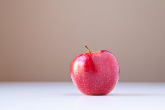 Single red apple on white table with taupe brown background. Concepts: nutrition, good food choices, balanced diet, good for you