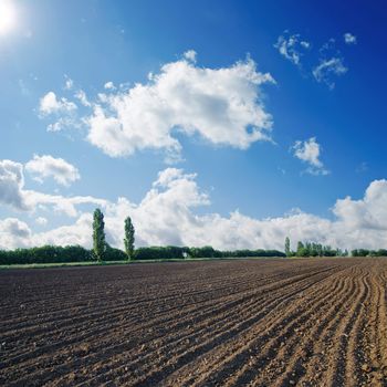 black ploughed field under blue sky with sun