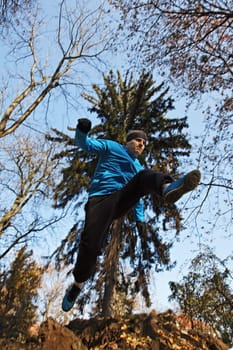Young man jumping over a hole in a forest.